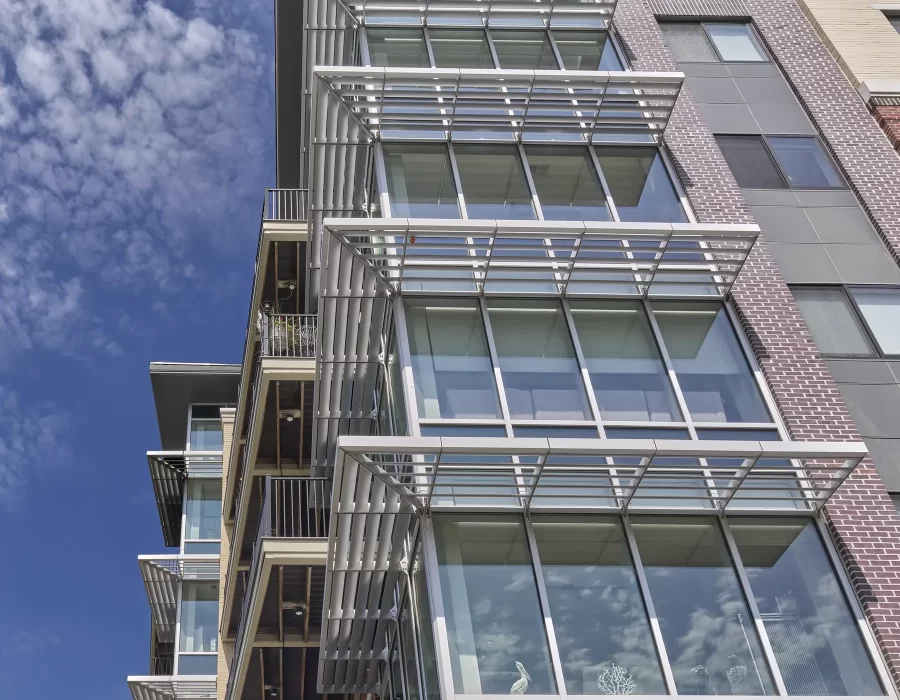 Upward view of a modern residential building with glass balconies and louvered sunshades against a blue sky