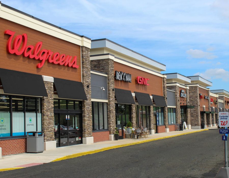 Strip mall storefront with Walgreens, GNC, Brew Haha, and jewelry shop signage under a stone and wood facade