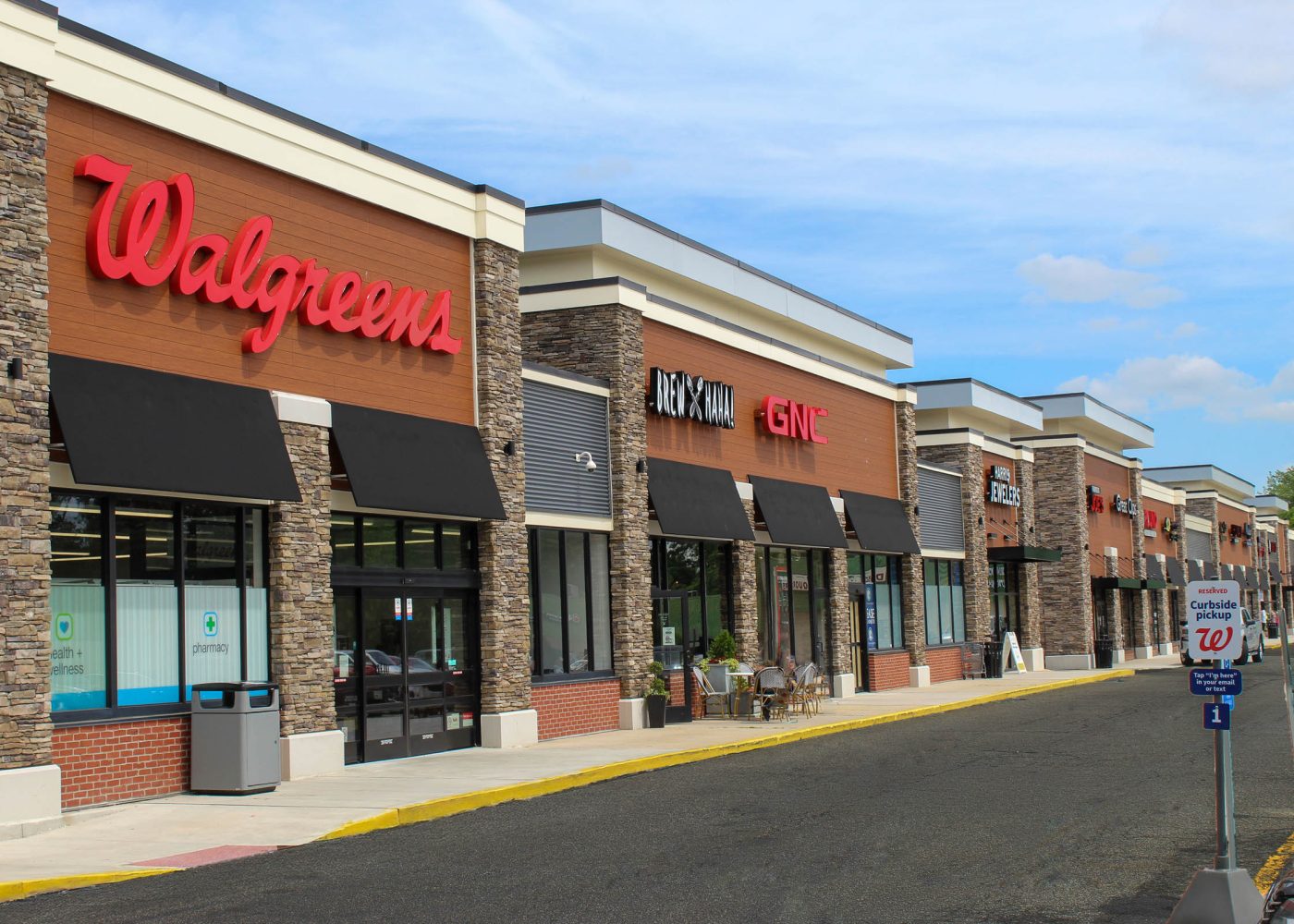 Strip shopping center exterior with Walgreens, GNC, Brew Haha, and Harris Jewelers storefronts under a blue sky.