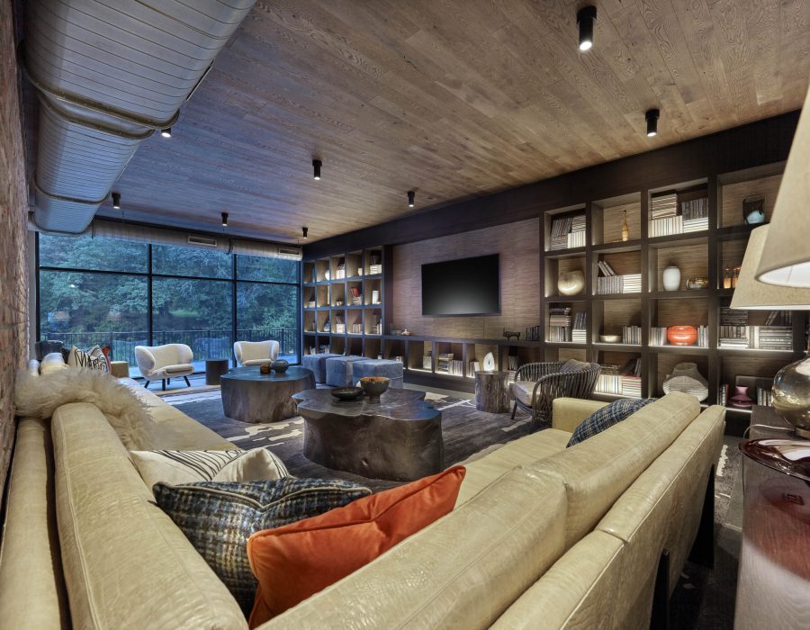 Lounge with leather sofas, built-in bookshelves, wall-mounted TV, and floor-to-ceiling windows overlooking trees