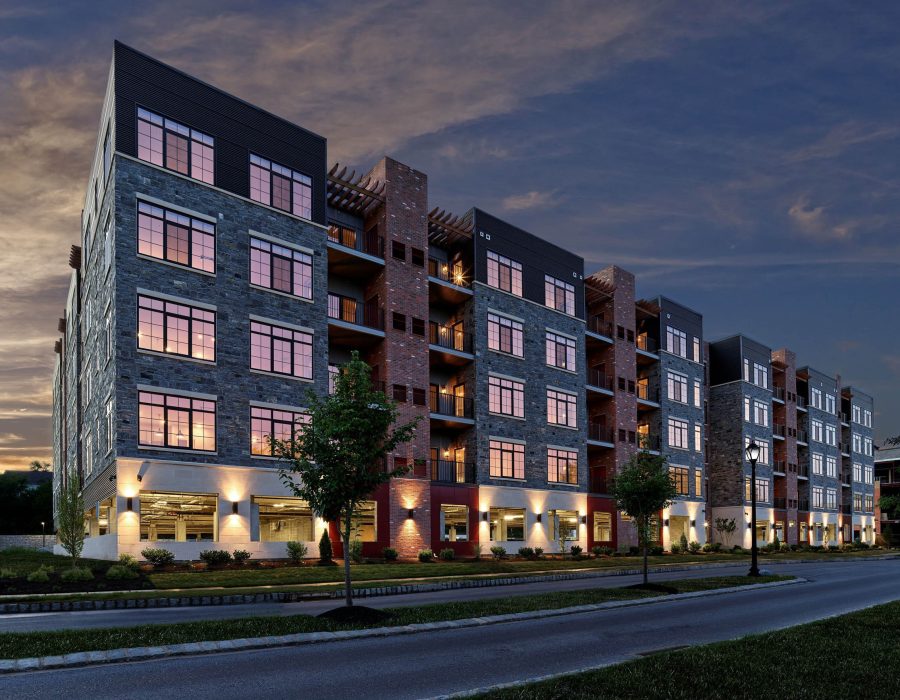 Multi-story apartment building with stone and brick facade illuminated at dusk, featuring large windows and balconies
