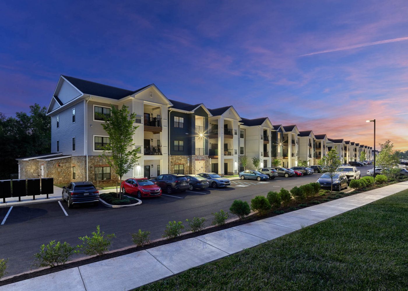 Three-story apartment building with illuminated exteriors and a parking lot at twilight