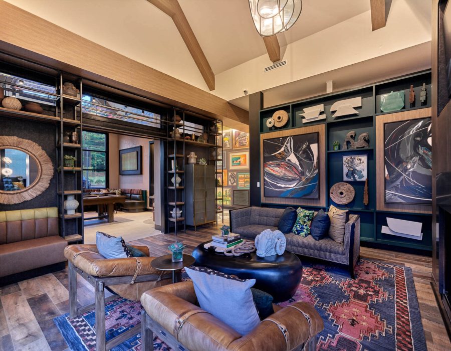 Lounge area with leather chairs, patterned rug, built-in shelving and layered artwork beneath exposed wood beams