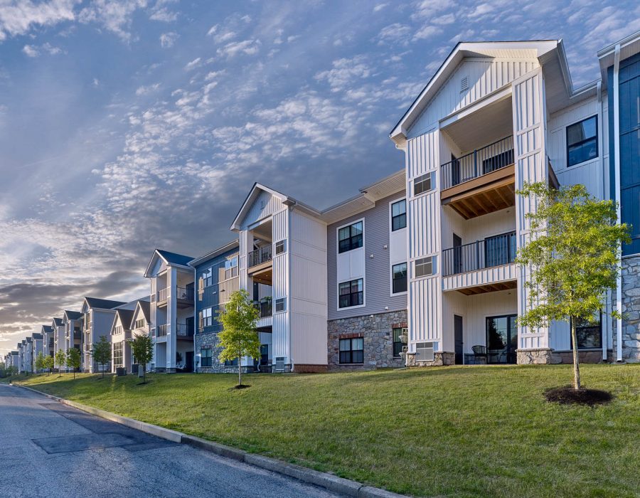 Row of three-story apartment buildings with balconies and stone accents along a curved street under a blue sky