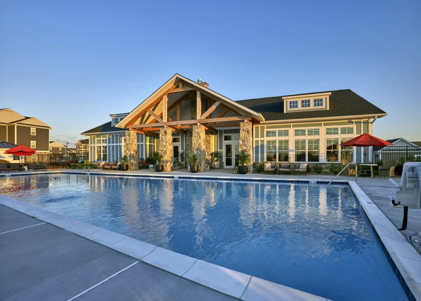 Rectangular pool with red umbrellas in front of a clubhouse featuring a timber-frame porte-cochere entrance