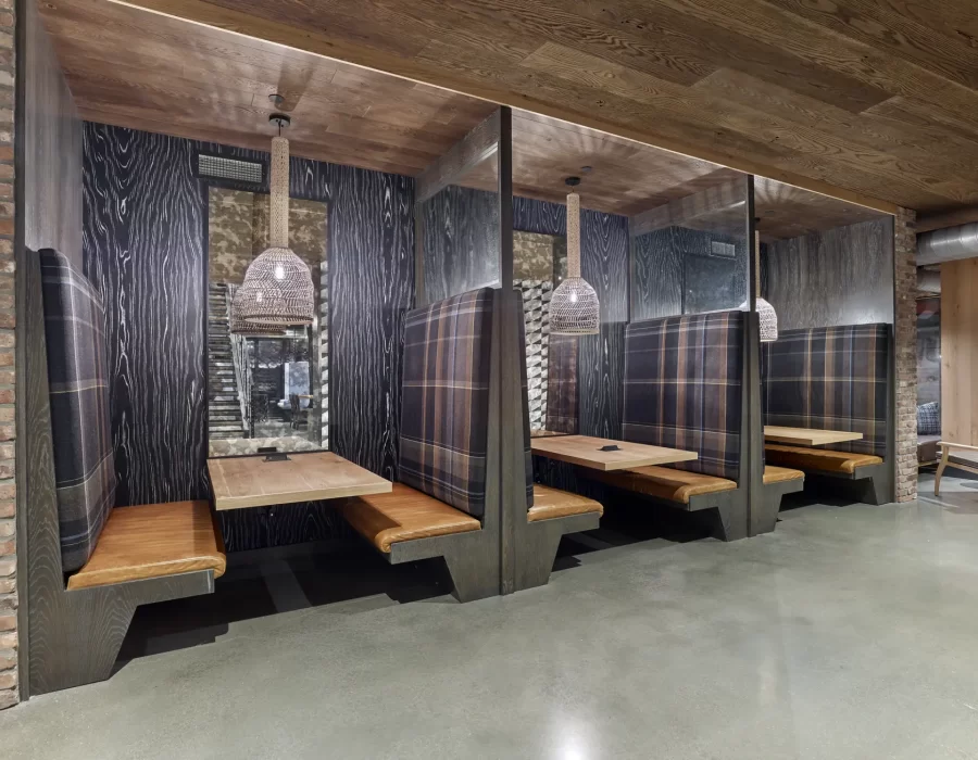 Row of enclosed plaid booth seating with wood tables and woven pendant lights in a restaurant interior