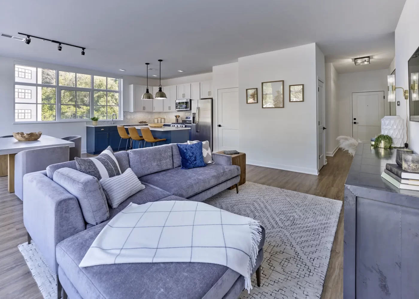 Open-concept living room with gray sectional sofa, patterned rug, and kitchen with blue cabinetry in background