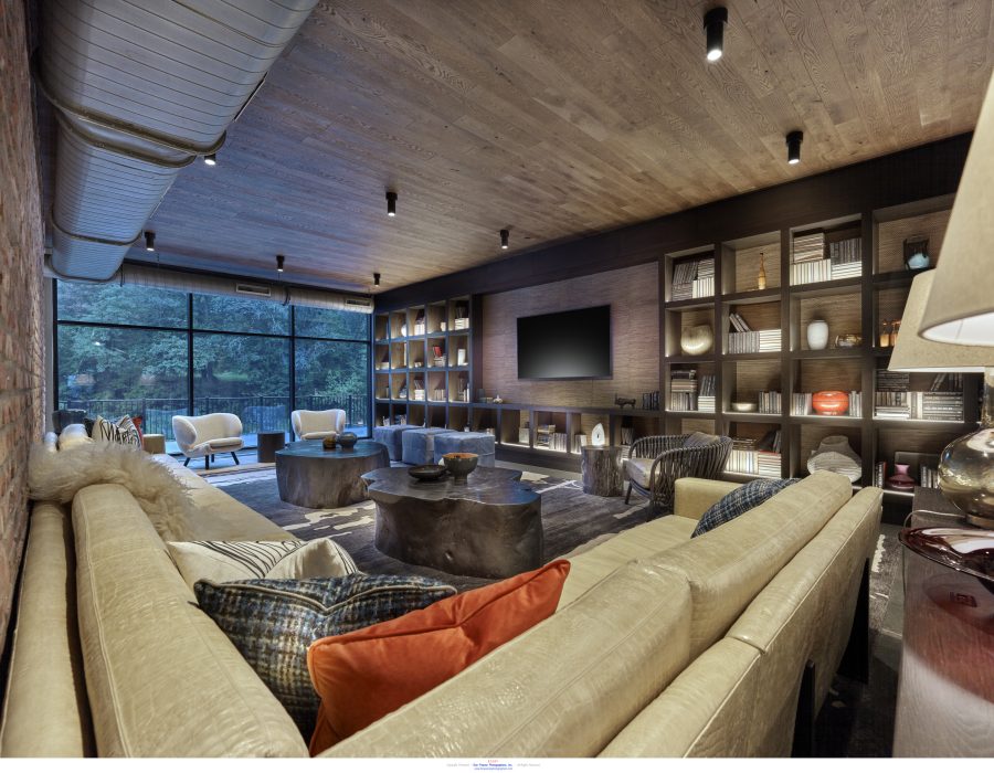 Modern living room with leather sofas, built-in bookshelves, wall-mounted TV, and floor-to-ceiling windows overlooking trees