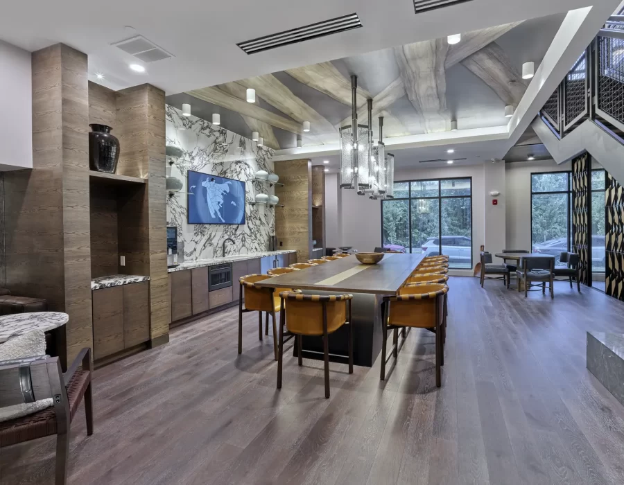 Community lounge with long communal table, wood flooring, marble accent wall, and staircase to upper level