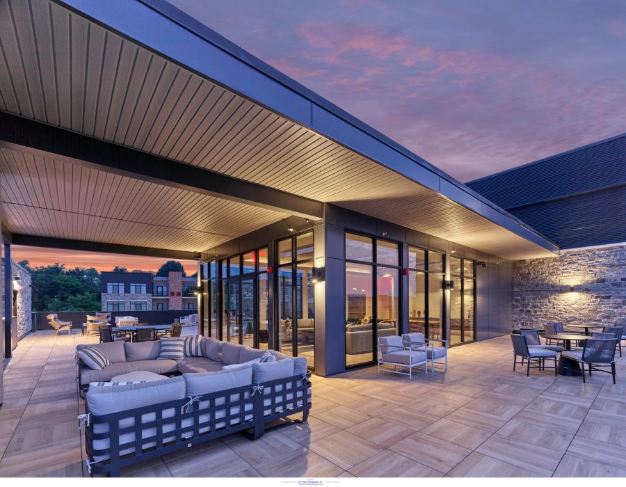 Rooftop terrace lounge with sectional sofas and dining tables under a sleek overhang at sunset