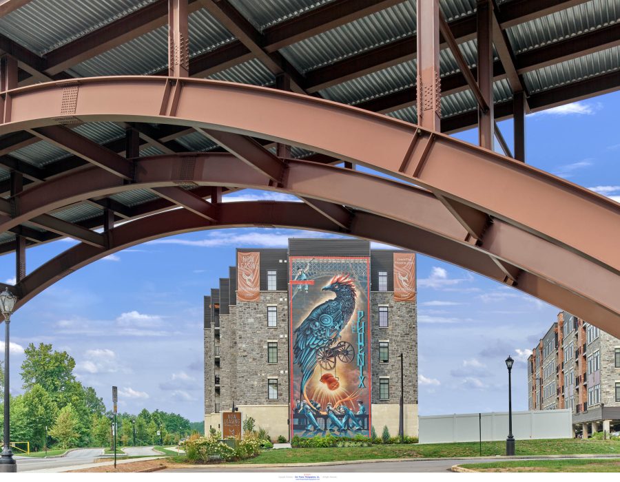 Stone apartment building with a large phoenix mural, viewed beneath an arched metal canopy structure