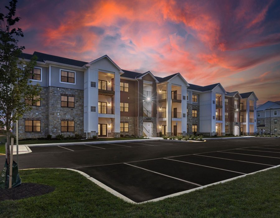 Three-story apartment building with stone and siding exterior, empty parking lot, under a vivid sunset sky